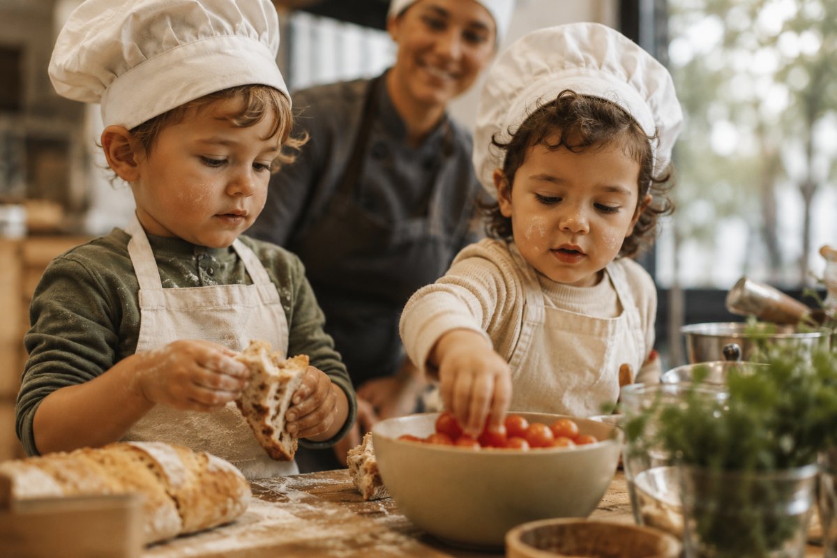 Two small children in aprons preparing food with a chef